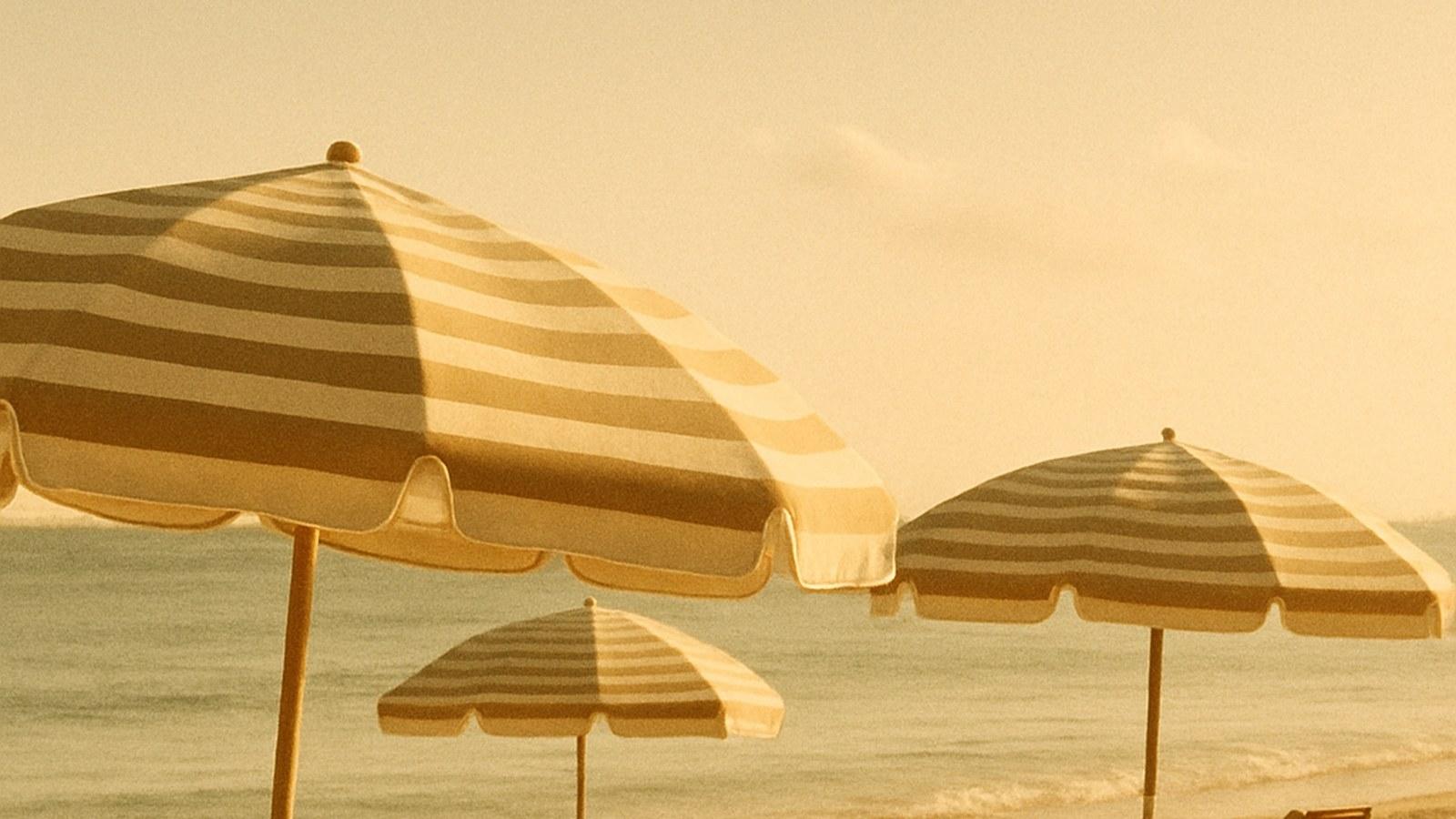 Vintage striped beach umbrellas and wooden loungers on golden Miami Beach sand, 1940s